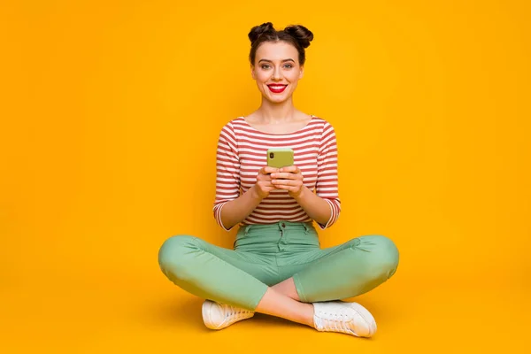 Foto em tamanho completo de atraente senhora sentar pernas chão cruzado segurar telefone verificar novos seguidores assinantes usar listrado vermelho branco camisa verde calças sapatos isolado amarelo cor fundo — Fotografia de Stock