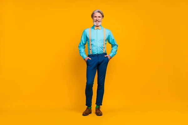 Pleine longueur photo de cool à la mode papy tenir les mains poches personne charismatique look élégant vêtements porter chemise bretelles noeud papillon pantalon bottes chaussettes isolé couleur jaune fond — Photo