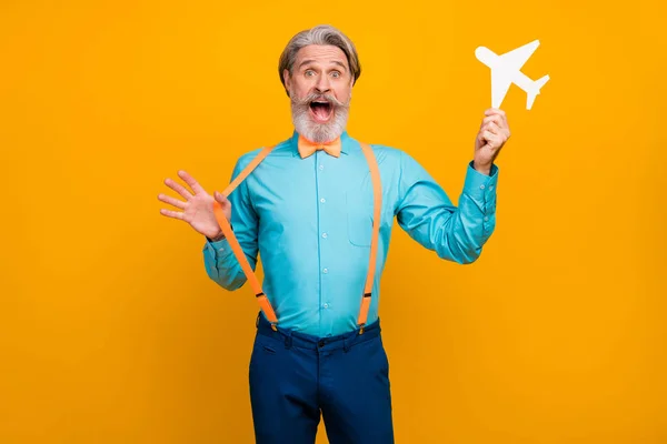 Foto do vovô legal segurar avião de papel recomendo nova companhia aérea show voando bom humor desgaste azul camisa suspensórios arco gravata calças isolado cor amarela fundo — Fotografia de Stock