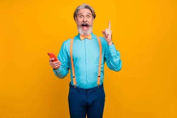 Photo de papy branché tenir les mains du téléphone personne intelligente lever le doigt excellente idée pour le nouveau post porter bretelles chemise bleue noeud papillon pantalon isolé couleur jaune fond — Photo