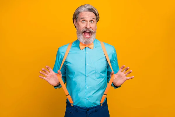 Foto de roupas legais bonito vovô espantado bom humor pronto para festa arrepiante comemorando desgaste camisa azul suspensórios arco gravata isolado cor amarela fundo — Fotografia de Stock