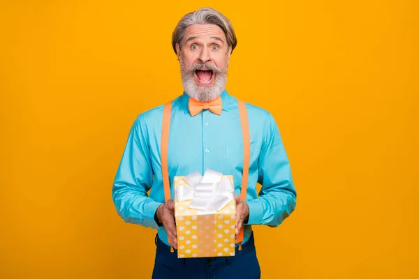 ¿Es para mí? Foto de Funky loco gris pelo abuelo celebrar regalo grande caja de cumpleaños sorpresa asombrado boca abierta usar camisa azul tirantes lazo de lazo aislado color amarillo fondo —  Fotos de Stock