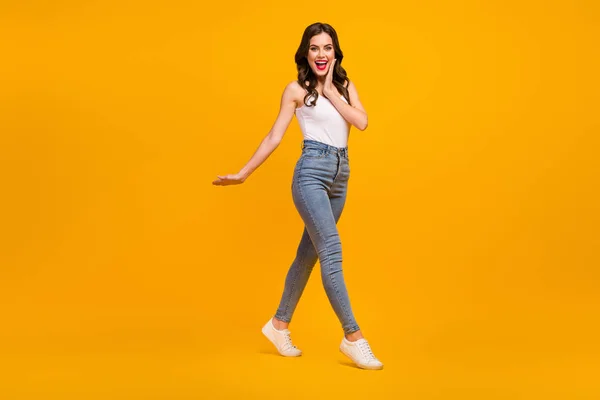 Full body profile photo of attractive cheerful lady good mood walk street arm on cheek wear white tank-top jeans footwear isolated bright yellow color background — 스톡 사진