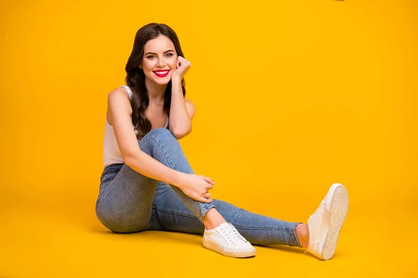 Full length photo of pretty cheerful lady sit floor cozy dreamy lean head on hand addicted traveler wear white tank-top jeans shoes isolated bright yellow color background — Stock fotografie