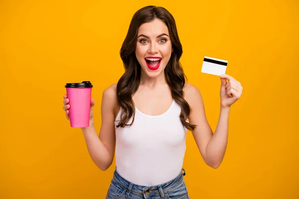 Photo of funny pretty lady hold paper takeout coffee cup plastic credit card buy beverage without cash wear white tank-top jeans isolated bright yellow color background — Stock Fotó