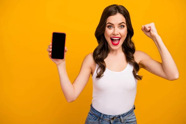 Photo of funny pretty lady telephone hand showing screen new gadget model low season price advertisement wear white tank-top jeans isolated bright yellow color background — Stock Photo, Image