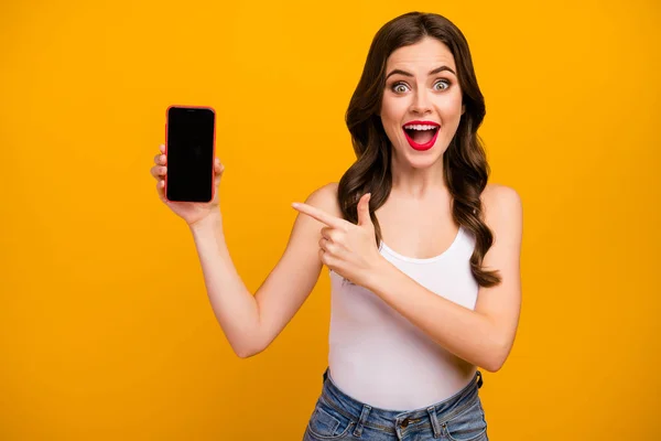 Photo of surprised funny lady telephone hand indicate finger screen advertising new gadget model low price wear white tank-top jeans isolated bright yellow color background — Φωτογραφία Αρχείου