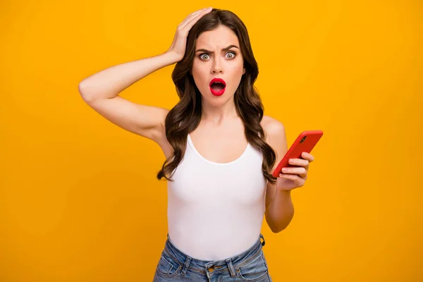Photo of pretty shocked speechless lady hold telephone open mouth read bad news hand on head wear white tank-top jeans isolated bright yellow color background — 图库照片