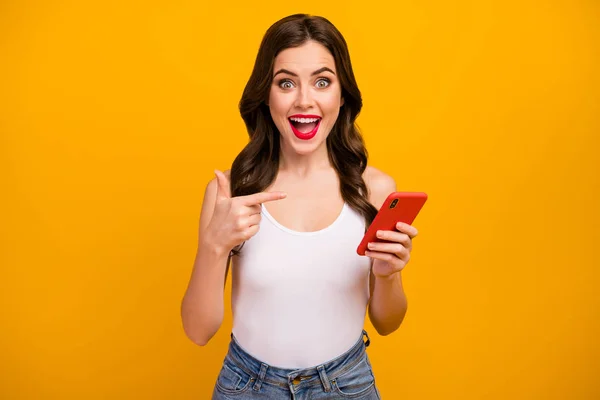 Photo of pretty lady hold telephone hands open mouth directing finger device presenting cool wifi connection wear white tank-top jeans isolated bright yellow color background — Stock Fotó
