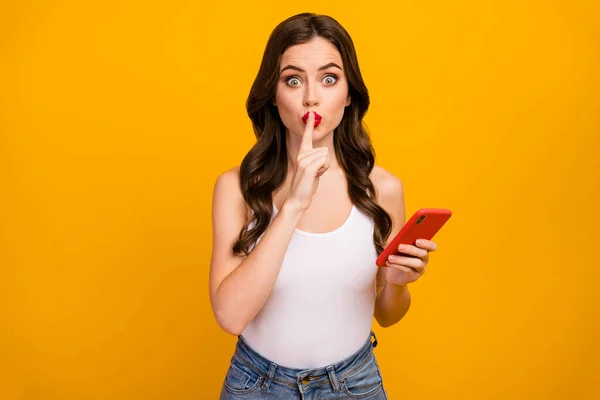 Dont speak Photo of pretty lady hold telephone hands hold finger on red lipstick lips influencer wear white tank-top jeans isolated bright yellow color background — Stock Fotó