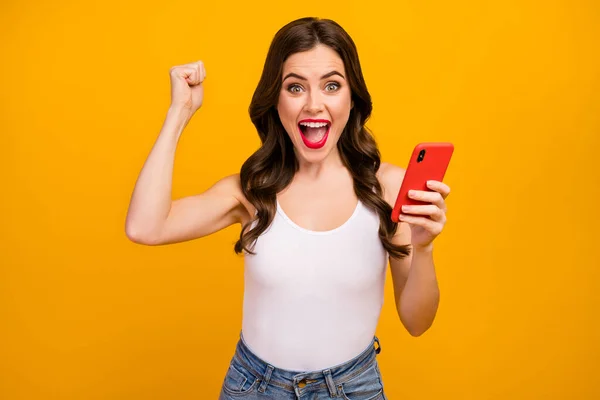 Photo of crazy funny lady hold telephone hands raise fist excited mood got many likes reposts comments wear white tank-top jeans isolated bright yellow color background — Stock Fotó