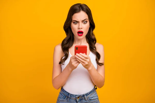 Photo of pretty shocked lady speechless expression hold telephone hands open mouth read bad news wear white tank-top jeans isolated bright yellow color background — 图库照片