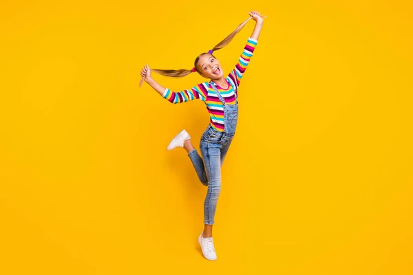 Full size photo of candid dreamy child enjoy fall weekends holidays touch her pigtails laugh rejoice wear sweater footwear isolated over yellow color background — Stockfoto