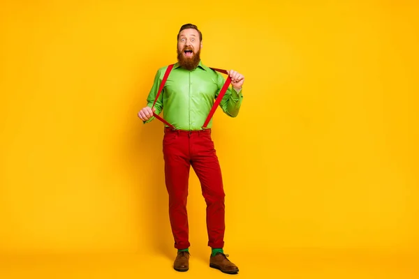 Full body photo of attractive funny guy model good mood playful macho wear green shirt red suspenders pants socks footwear isolated vibrant color background — Stock fotografie