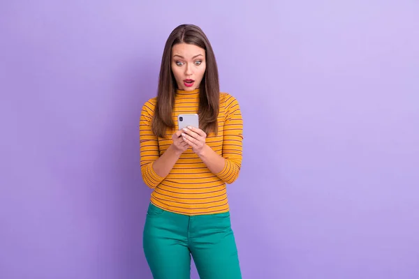 Portrait of crazy astonished girl social network user use smart phone read comment feedback impressed scream wow omg wear good look jumper trousers isolated over purple color background — Stock Fotó