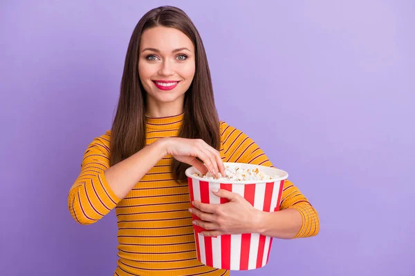 Portrait of charming lovely cute sweet girl hold pop corn striped box eat watching interesting film wear casual style good look sweater isolated over violet purple color background — Stockfoto