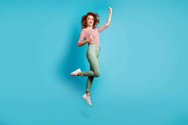 Full body profile photo of funny lady jump high raise fists win sportive championship celebrating wear casual red white shirt green pants shoes isolated blue color background — ストック写真