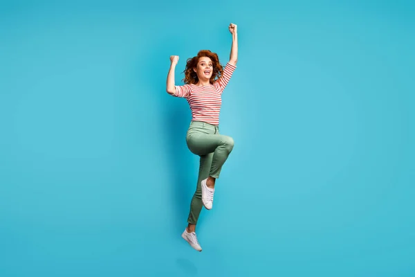 Full body profile photo of funny lady jump high raise fists win sports competition championship wear casual red white shirt green pants shoes isolated blue color background — 图库照片