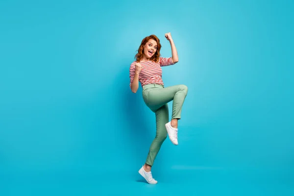 Yeah. Full length profile photo of beautiful lady crazy emotions raise fists win money lottery wear casual red white shirt green pants footwear isolated blue color background — Zdjęcie stockowe