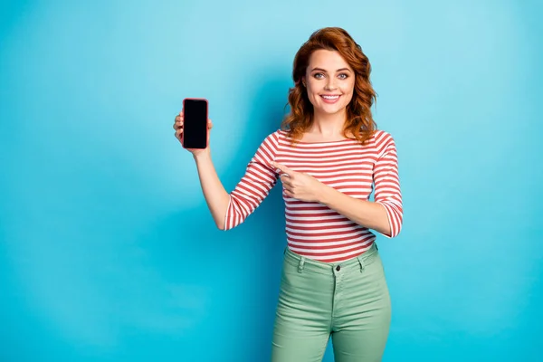 Portrait of positive cheerful woman promoter hold smartphone point index finger suggest select modern technology product promo wear casual style jumper isolated over blue color background — Zdjęcie stockowe