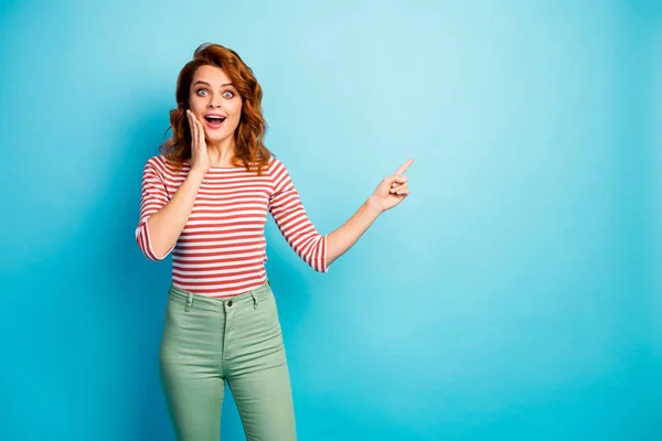 Omg look unbelievable ads. Astonished crazy woman point index finger copyspace indicate promo scream wow omg touch face hand wear white green jumper isolated over blue color background — Stockfoto
