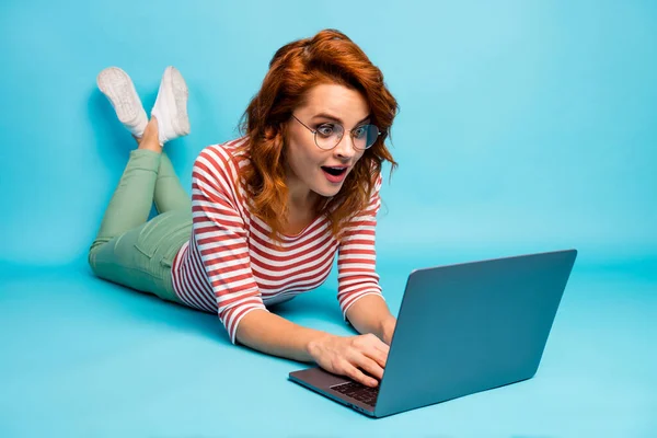 Full size close up photo crazy woman lie floor work laptop get incredible blogging notification impressed scream wow omg wear good look sneakers isolated blue color background — Zdjęcie stockowe