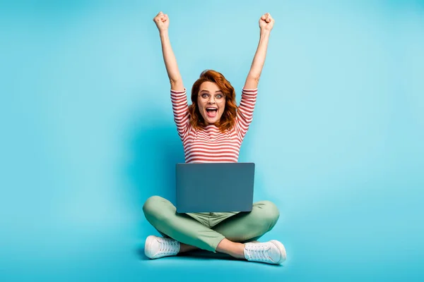 Foto em tamanho completo de mulher de cabelo de gengibre animado sentar pernas chão cruzado trabalho laptop terminar start-up relatório gritar sim levantar punhos desgaste verde branco suéter calçado isolado azul cor fundo — Fotografia de Stock