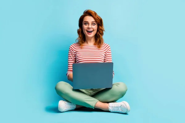 Full size photo of crazy astonished girl sit floor legs crossed work computer search job website impressed scream wow omg wear stylish outfit sneakers isolated over blue color background — Stockfoto
