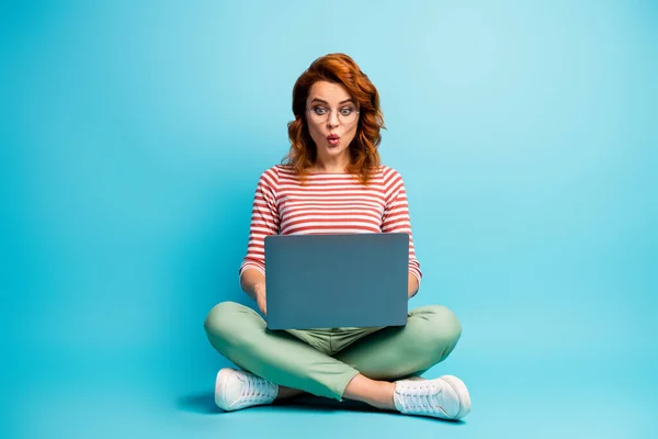Full length photo of astonished girl sit legs crossed work on computer read social media job information document impressed scream wow omg wear stylish outfit isolated blue color background — Zdjęcie stockowe
