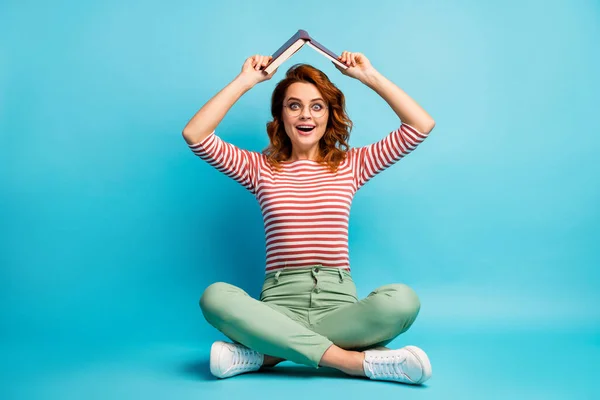 Comprimento total da foto louco menina surpreendido sentar pernas andar cruzado quer descanso relaxar colocar o livro de papel acima da cabeça impressionado gritar wow desgaste branco verde calças sapatos isolados azul cor fundo — Fotografia de Stock