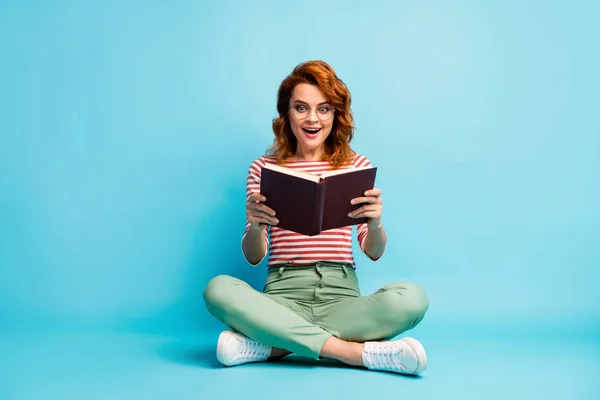 Full length photo of crazy book worm woman sit floor rest relax cross legs read book impressed scream wow omg wear white green footwear pants isolated blue color background — 스톡 사진