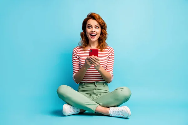 Foto em tamanho completo de entusiasmado menina assentado pernas cruzadas uso celular ler rede social notícias impressionado grito wow omg usar sapatos brancos verdes isolados sobre fundo de cor azul — Fotografia de Stock