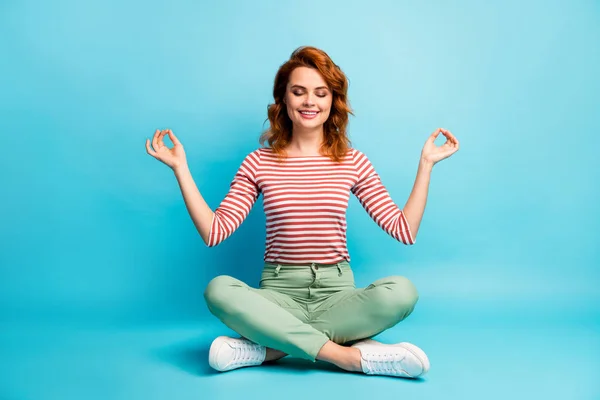 Full body photo of positive calm woman sit crossed legs meditate yoga show om symbol wear white shoes outfit isolated over blue color background — Stock fotografie