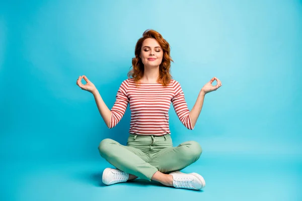 Full size photo of quiet serene woman sit floor crossed legs show om sign exercise yoga meditation wear stylish green outfit isolated over blue color background — Stock fotografie