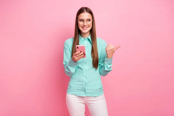 Retrato de chica alegre positiva utilizar el teléfono celular presente anuncios en las redes sociales punto de promoción copyspace dedo índice usar traje de pantalones blancos verde aislado sobre fondo de color pastel —  Fotos de Stock