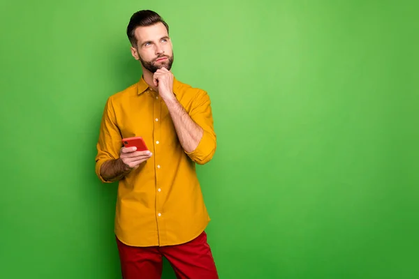 Retrato de sua ele agradável atraente sério cara de mente na camisa formal segurando na célula da mão pensando criando ideia smm isolado no brilhante brilho vívido cor verde vibrante fundo — Fotografia de Stock