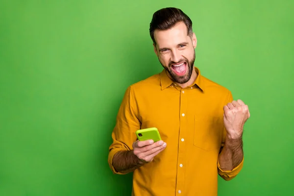 Portrait of nice attractive cheerful cheery satisfied guy in formal shirt using cell celebrating winning great luck isolated on bright vivid shine vibrant green color background — 图库照片