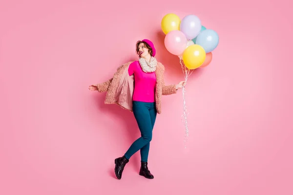 Full length photo of pretty lady traveler hold colorful air balloons surprise birthday party wear fur coat garment scarf beret cap sweater pants shoes isolated pink color background