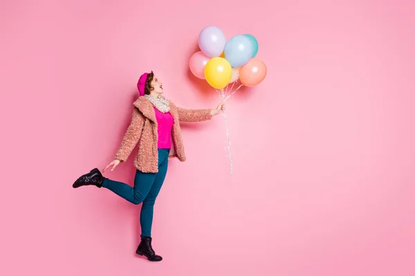 Foto de tamaño completo de la señora bonita divertida sostienen muchos globos de colores volando hasta el aire loco sorpresa desgaste de moda abrigo de piel bufanda gorra pantalones zapatos aislados de color rosa fondo — Foto de Stock