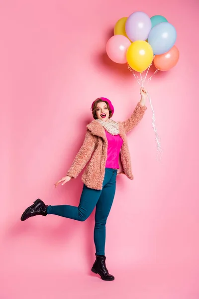 Foto vertical de cuerpo completo de la señora modelo divertido sostienen muchos globos de colores volando hasta la boca abierta de aire desgaste moderno abrigo de piel bufanda boina gorra pantalones zapatos aislados de color rosa fondo —  Fotos de Stock