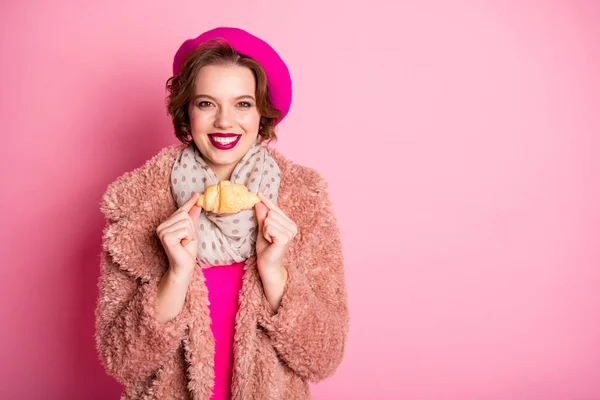 Φωτογραφία του όμορφου ταξιδιώτη κυρία κρατήσει φρέσκο κρουασάν πρωινό σνακ στο εξωτερικό ταξίδι φορούν casual κομψό γούνα κασκόλ μπερέ καπέλο ρούχα στολή απομονωμένο ροζ χρώμα φόντο — Φωτογραφία Αρχείου
