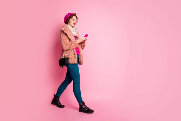 Full storlek foto av ganska resenär dam hålla telefon chatta vänner gå ner gatan slitage casual elegant päls jacka halsduk byxor skor outfit isolerad rosa färg bakgrund — Stockfoto