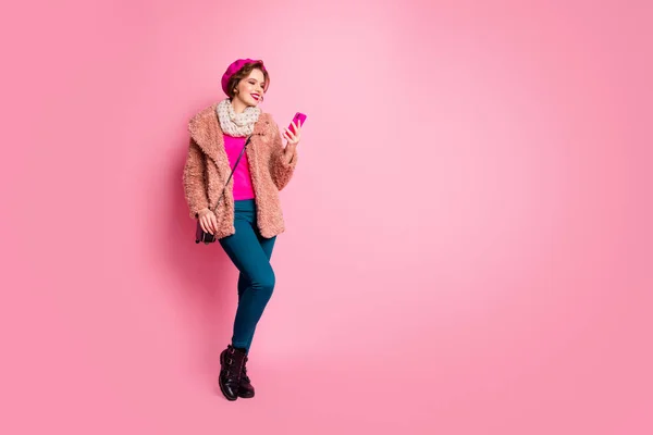 Helkroppsfoto av söt dam hålla telefon chatta vänner gå ner gatan slitage casual elegant fjäder päls halsduk byxor skor koppling outfit isolerad rosa färg bakgrund — Stockfoto