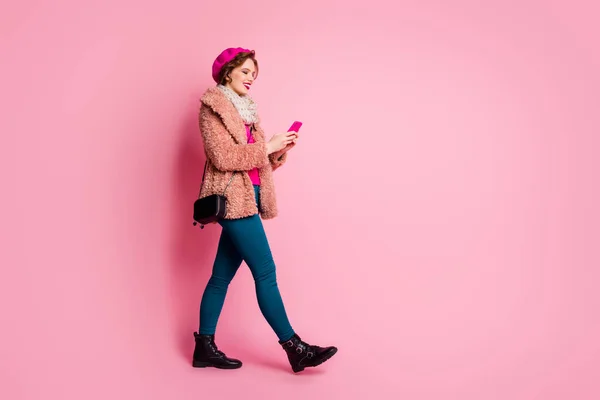 美女拿着电话聊天的朋友走在街上，穿着休闲时髦的皮大衣围巾贝雷帽长裤套装孤立的粉色背景 — 图库照片