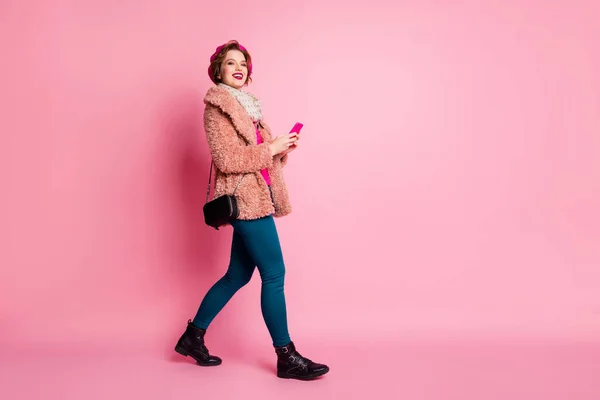 Full längd profil foto av vackra dam hålla telefon chatta vänner promenader ner gatan slitage casual elegant päls jacka halsduk byxor skor isolerad rosa färg bakgrund — Stockfoto