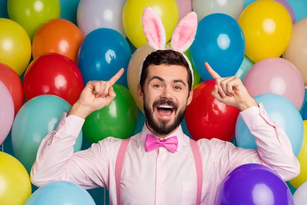 Foto von lustigen coolen Kerl bunte Dekor Ostern festliche Partystimmung direkte Finger Kopf tragen rosa Hemd Fliege Strapse flauschige Hasenohren auf Luftballons kreatives Design Hintergrund — Stockfoto