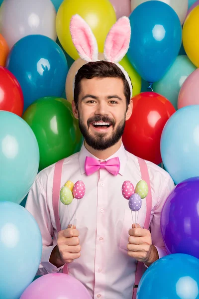 Frohe Ostern. Vertikale Foto von lustigen Kerl bunte Dekor Party festliche Stimmung halten Eier Sticks tragen rosa Hemd Fliege Strapse flauschige Hasenohren auf Luftballons kreativen Hintergrund — Stockfoto