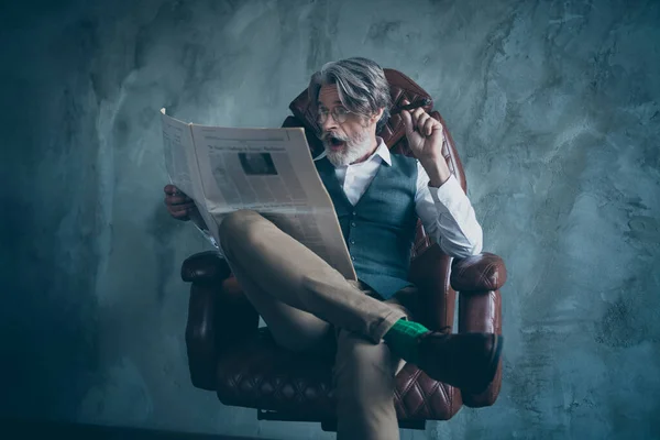 Omg world economy change. Crazy luxury chic classy old man company owner sit armchair hold cigar read magazine scream wow impressed wear grey shirt pants vest isolated concrete wall background