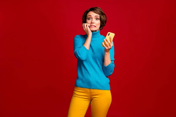 Πορτρέτο της απογοητευμένης blogger χρήση smartphone αισθάνονται ανήσυχος συναισθήματα περιμένουν αρνητικά σχόλια social media δαγκώσει τα νύχια φορούν λάμψη κομψό πουλόβερ απομονωμένο κόκκινο χρώμα φόντο — Φωτογραφία Αρχείου