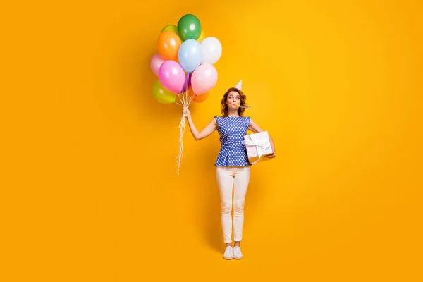 Ganzkörperfoto der hübschen Dame halten bunte Luftballons große Geschenkbox Party Schlag Noisemaker tragen Papier Kegelhut Tupfen blaues Hemd weiße Hose Schuhe isoliert gelbe Farbe Hintergrund — Stockfoto